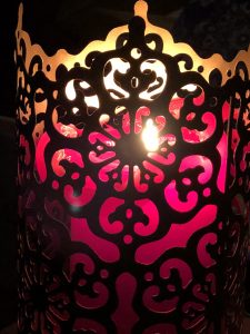 lit red candle in a tall brass holder with cutouts, all on a dark background